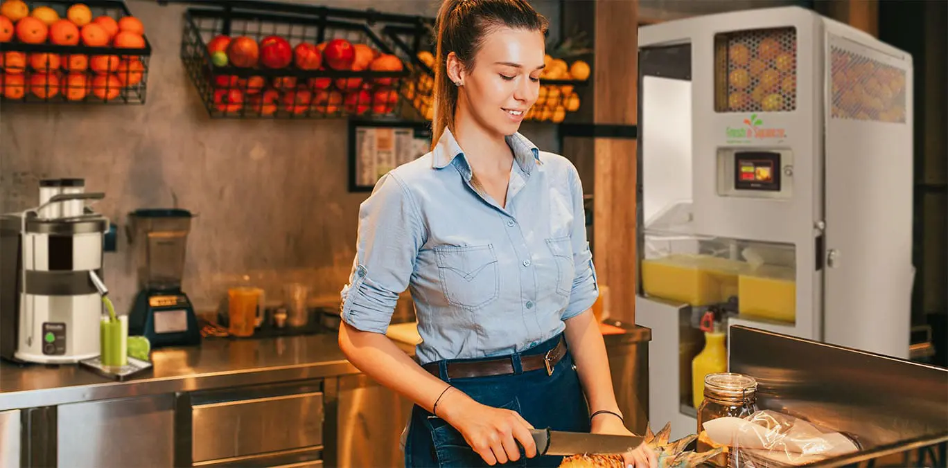 Server working in a juice bar that is part of a grocery store she is making orange juice while slicing pineapple.